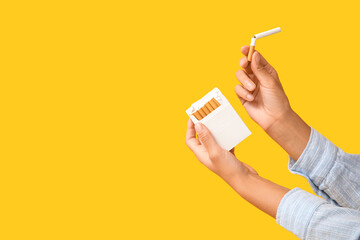 Female hands with pack of cigarettes on yellow background. Stop smoking concept