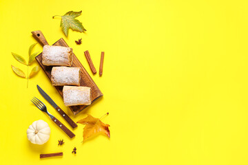 Wooden board with cut tasty pumpkin strudel, cinnamon and autumn leaves on yellow background