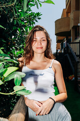 A young woman stands among lush green leaves, her hair flowing in the breeze, exuding confidence and natural beauty