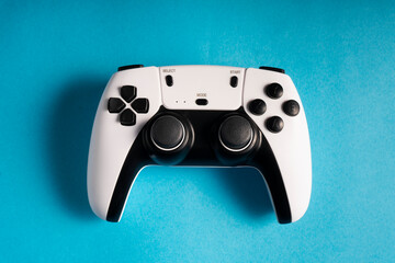 A white and black gaming controller is centered on a bold cyan background. The buttons, joysticks, and modern design stand out, creating a striking contrast that highlights the device's sleek look.