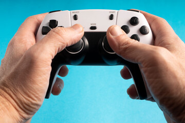 Two hands firmly grips a white and black gaming controller against a bright cyan background. The buttons, joysticks, and design details are clearly visible, emphasizing a modern gaming experience.