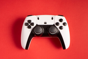 A white and black gaming controller is centered on a bold red background. The buttons, joysticks, and modern design stand out, creating a striking contrast that highlights the device's sleek look. © P10NERO