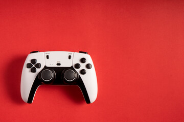 A white and black gaming controller is a corner on a bold red background. The buttons, joysticks, and modern design stand out, creating a striking contrast that highlights the device's sleek look.