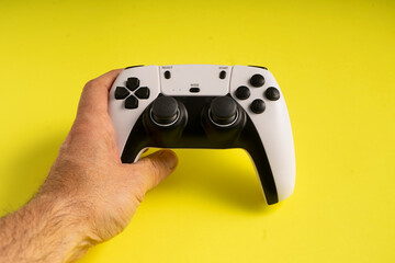 A hand firmly grips a white and black gaming controller against a bright yellow background. The buttons, joysticks, and design details are clearly visible, emphasizing a modern gaming experience.