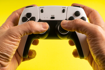 Two hands firmly grips a white and black gaming controller against a bright yellow background. The buttons, joysticks, and design details are clearly visible, emphasizing a modern gaming experience.