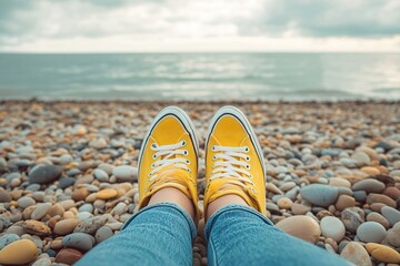 Obraz premium Coastal Relaxation: Feet in Yellow Canvas Shoes on Pebble Beach by Ocean Waves