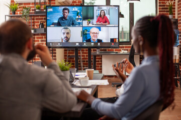Workers in office discussing strategy ideas with colleagues through a virtual meeting platform on screen. Entrepreneurs participate in online call, collaborating on marketing plan in video webinar.