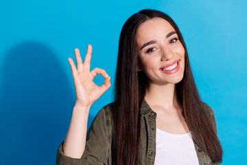 Smiling young woman making okay gesture in front of blue background, expressing positive emotions...