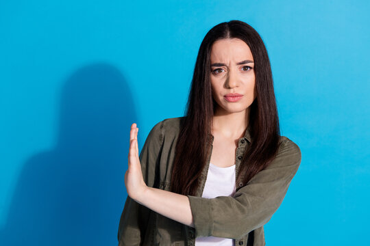 Confident young woman gesturing stop with hand against a vivid blue backdrop, expressing refusal and assertiveness