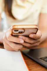 Hands holding a smartphone over a desk with a laptop and notebook, depicting multitasking in a...