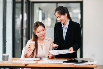 Two professional women in a modern office setting, collaborating over documents and coffee, showcasing teamwork and business strategy.