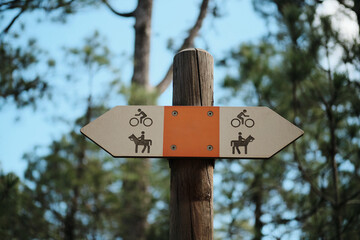 Rustic wooden signpost in forest points the way for cyclists and horseback riders.Perfect for travel,nature,or outdoor recreation themes.Orange and white color scheme eye-catching and simple.Tenerife
