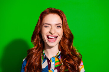 Young woman with a playful smile and winking gesture wearing colorful blouse on green background