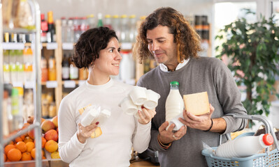Husband and wife choose natural farm dairy products. Married couple buying a set of milk, cheese and yogurt from a farm shop