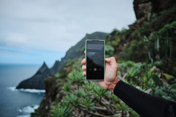 Person taking a photo of stunning coastal cliffs and ocean with a smartphone. Breathtaking landscape view from a high vantage point. Perfect for travel, adventure, and nature themes.
