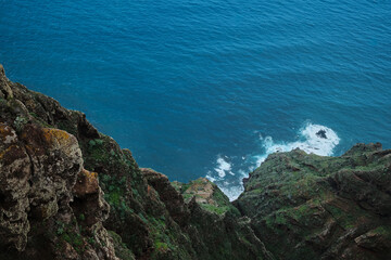Dramatic cliffside view overlooking a vibrant blue ocean.  Waves crash against the rugged rocks, creating a stunning coastal scene. Perfect for travel, nature, or adventure themes.