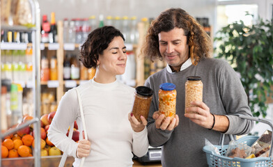 Couple choose for canned beans and lentils. European shoppers holding a jar of beans in his hands