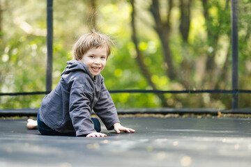 Little boy jumping on a trampoline in a backyard on warm and sunny summer day. Sports and exercises for children. Summer outdoor leisure activities.