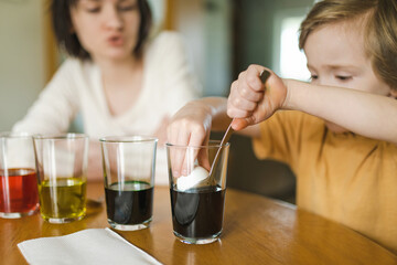 Big sister and her little brother dyeing Easter eggs at home. Children painting colorful eggs for Easter hunt. Kids getting ready for Easter celebration.