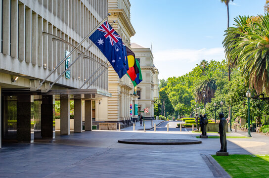 Treasury Place in East Melbourne, home to Victorian Government offices, with the Australian flag and Aboriginal flag displayed prominently on the historic building's facade.