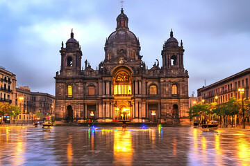 Obraz premium Grand Cathedral Illuminated at Twilight Reflects in Wet Plaza Beautifully with Colorful Fountain