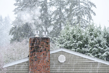 Snowing hard on a cold winter day, view of a brick chimney on a residential home with smoke from a...