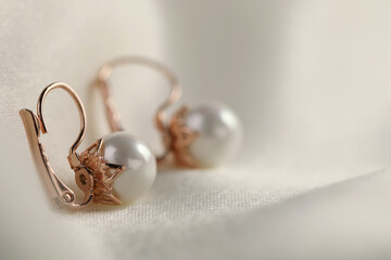 Beautiful pearl earrings on white silk, closeup. Space for text