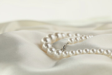 Beautiful pearl necklace on white silk, closeup