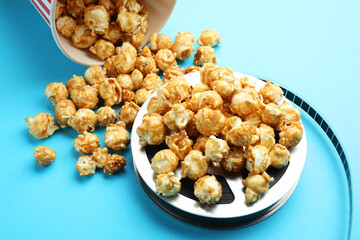 Sweet popcorn and film reel on light blue background, closeup. Watching movie