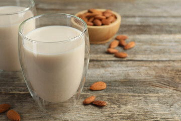Fresh nut milk in glasses and almonds on wooden table, closeup. Space for text