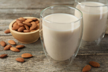 Fresh nut milk in glasses and almonds on wooden table, closeup