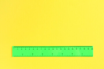 One green ruler on yellow background, top view. Space for text