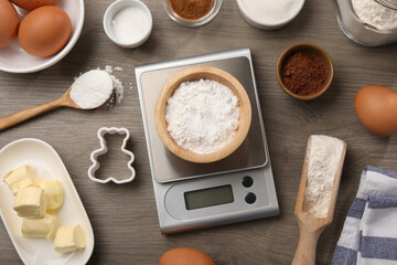Kitchen scale with bowl of baking powder and other products on wooden table, flat lay