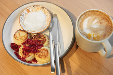 Delicious cottage cheese pancakes and tasty latte served on wooden table in cafe, closeup