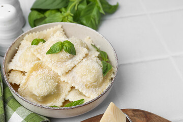 Delicious ravioli with cheese and basil served on white tiled table, closeup