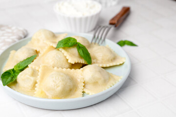 Delicious ravioli with cheese and basil served on white tiled table, closeup. Space for text