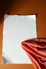 A blank white paper lies on a warm background, with soft pink fabric flowing below