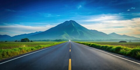 Asphalt road leading towards a majestic mountain range under a vibrant blue sky