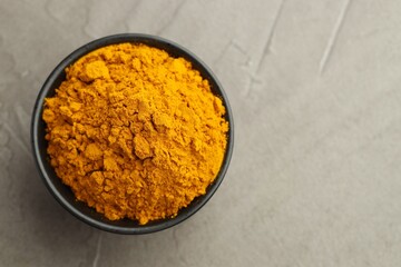 Turmeric powder in bowl on grey table, top view. Space for text
