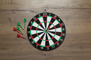 Dart board and colorful arrows on wooden background, flat lay