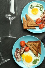Delicious fried eggs, bacon and pieces of toast served for brunch on black table, flat lay