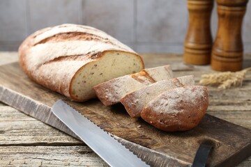 Cutting board with fresh bread, knife, spikes and shakers on wooden table, closeup