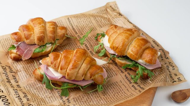 Croissant sandwich prepared with ham, serrano ham, arugula, cheese on a baking paper, healthy breakfast concept