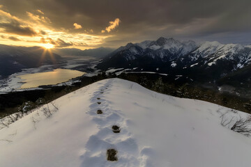 Obraz premium Footprints Lead Up a Snowy Mountain Ridge at Sunset Over a Valley