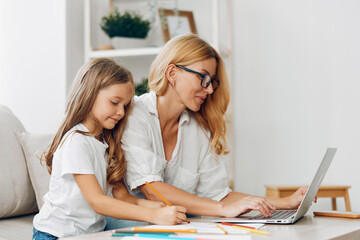 Mother and daughter bonding over creative drawing and learning with laptop and colored pencils at...