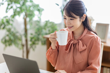 コーヒーを飲みながらパソコンを見る女性