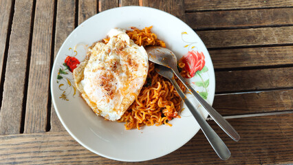 Indomie goreng Indonesian Popular Instant fried Noodle. Served with fried egg on wooden table. Copy Space for Text