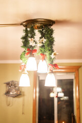 Ceiling light fixture decorated with garlands, flowers, and red bows for Christmas