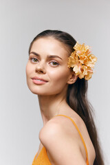 Fototapeta premium Portrait of a young woman with a floral accessory, showcasing natural beauty and soft expressions in a minimalist setting with neutral tones.