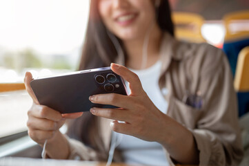 A happy Asian woman enjoys watching a movie on her smartphone on a bus, commuting in the city.